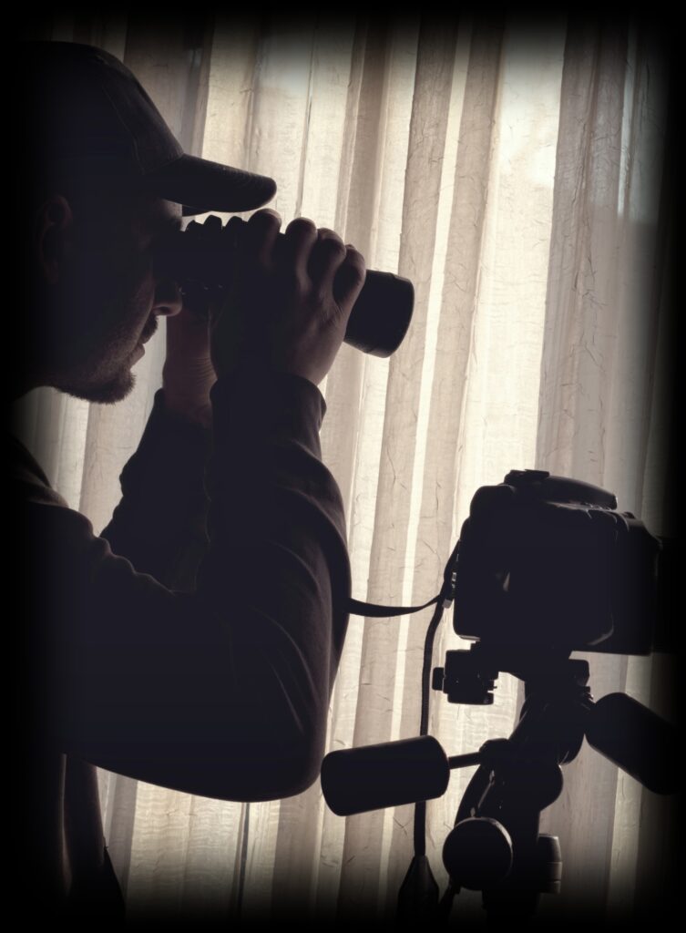 A covert surveillance operative looking through a pair of binoculars during an investigation